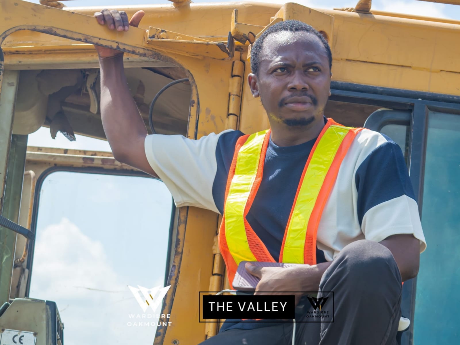 A man in a hi-vis vest crouches in the cab doorway of a yellow earth-moving machine, captioned 'The Valley' with Wardiere Oakmount branding.