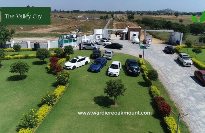 Aerial view of The Valley City estate entrance: a gatehouse, landscaped lawns and parked cars.